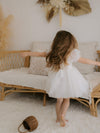 A young girl twirls wearing our Layla flower girl dress in light ivory.