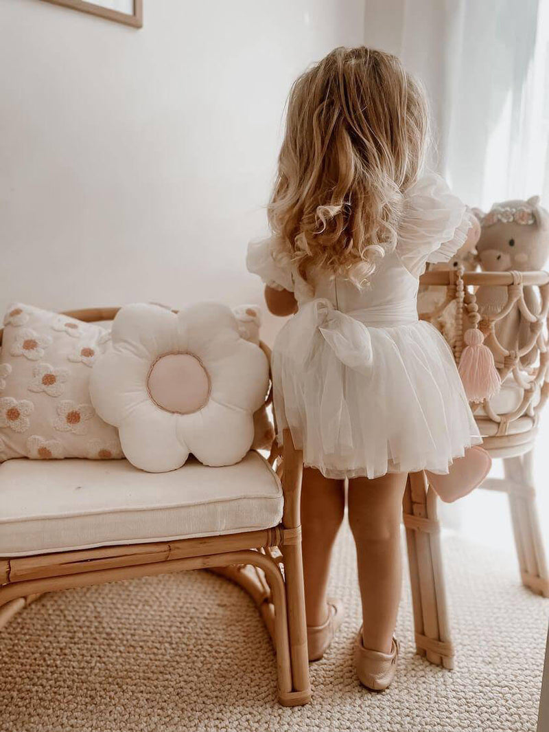 A young girl stands wearing our Layla flower girl romper dress in ivory.