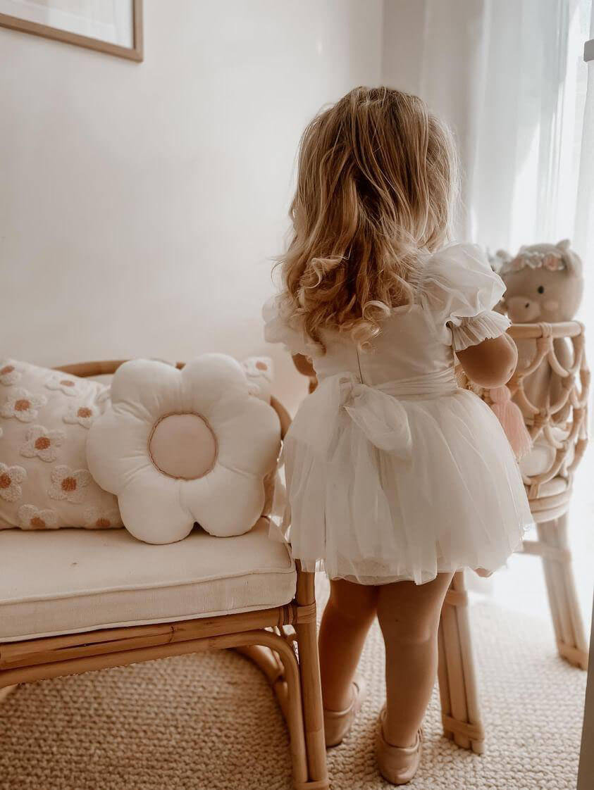 A toddler wears our ivory Layla flower girl romper as she plays with dolls.