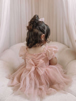 Layla champagne toddler flower girl dress is worn by a young girl, showing the back of the romper with a tulle bow.