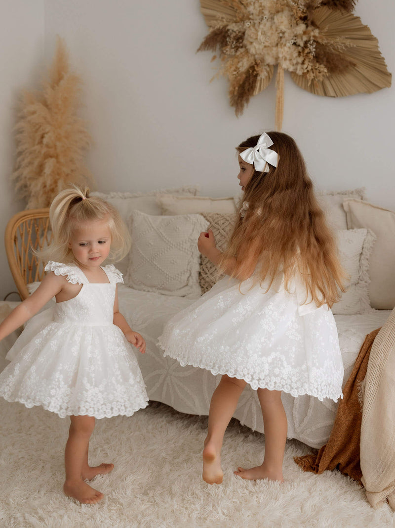 Two sisters twirl in our Loulou lace flower girl romper and matching Loulou lace flower girl dress.