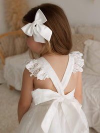 The back of our Loulou lace flower girl dress worn by a young girl. She is also wearing a girls ivory satin bow hair clip.