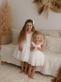 Two sisters stand wearing matching flower girl outfits. One wears our Loulou flower girl dress and the other wears the matching Loulou toddler flower girl romper.