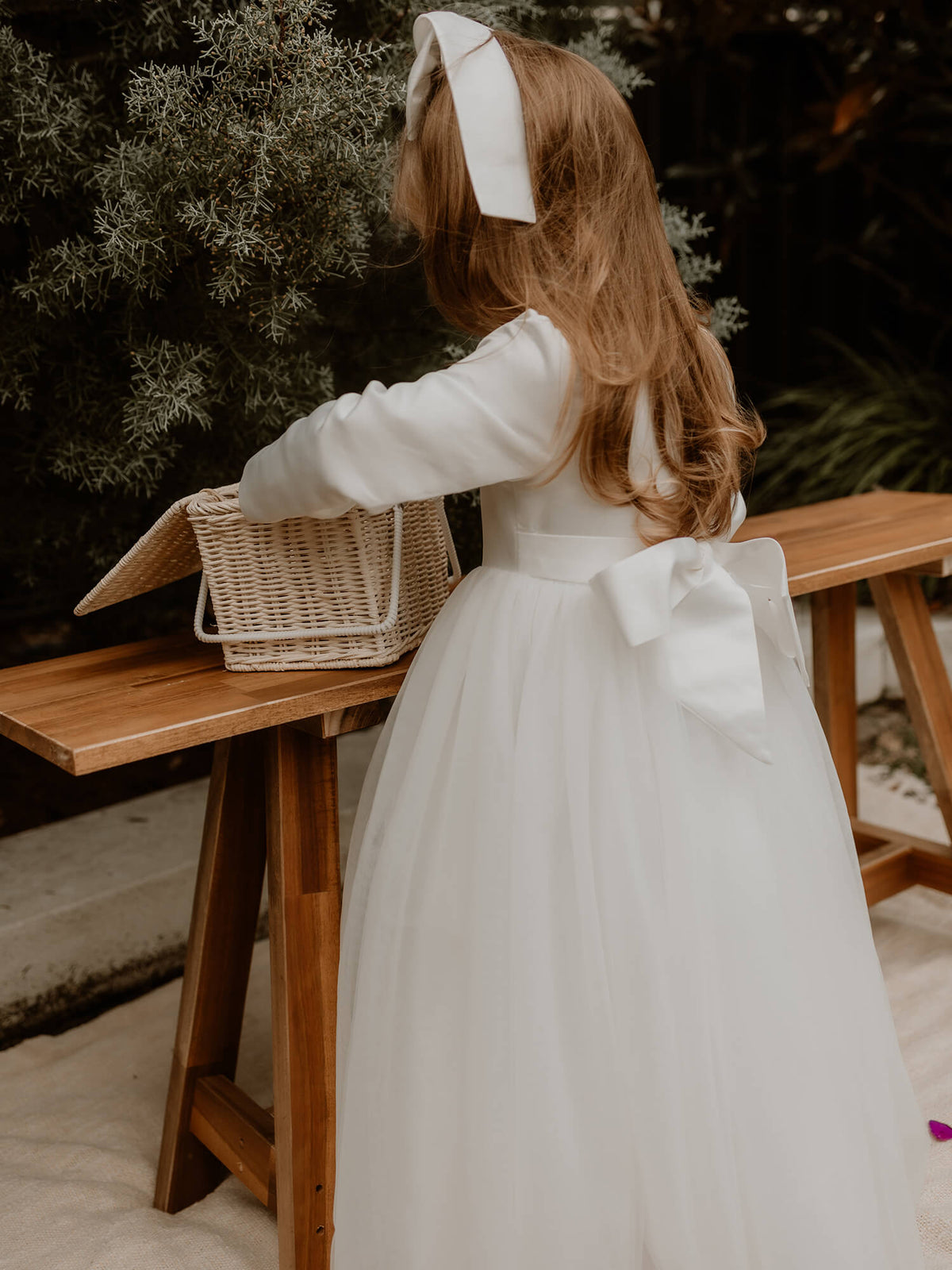 Winter flower girl dress, our Lucy dress, is worn by a young girl. Showing the satin bow at the back and matching satin bow girls hair accessory.