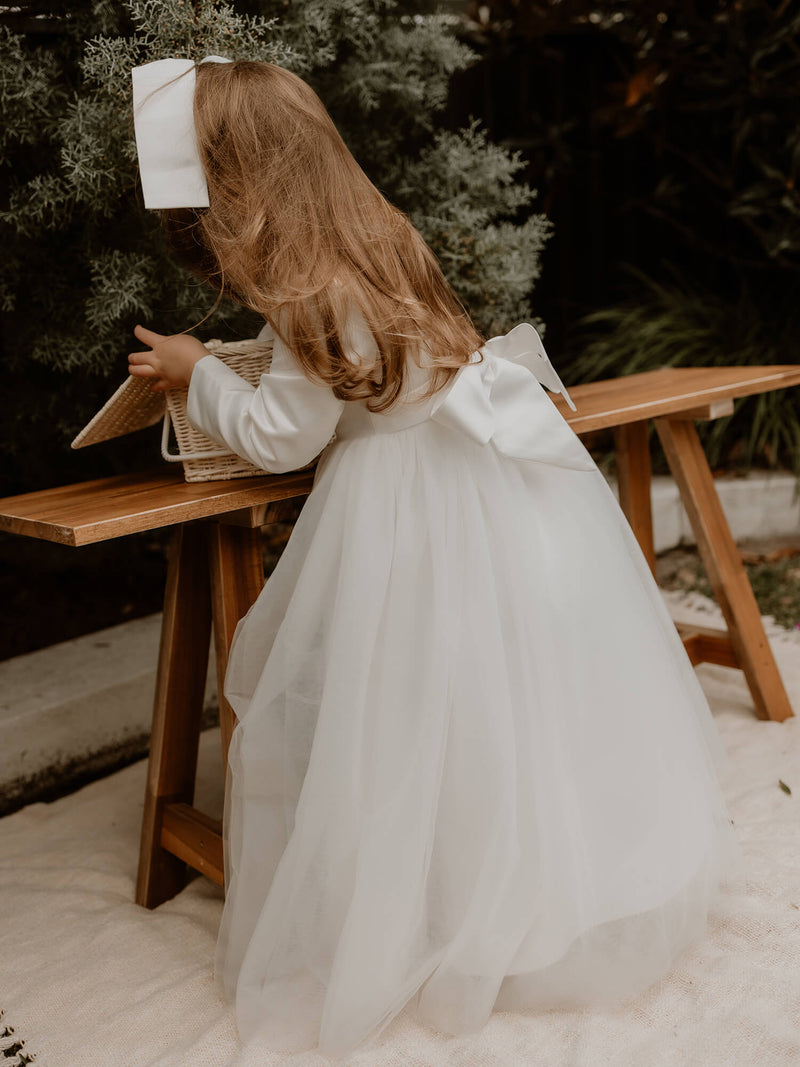 A young flower girl looks inside a basket, wearing our Lucy winter flower girl dress.