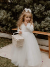 Lucy winter flower girl dress is worn by a young girl, she is holding a flower girl basket and has a satin bow in her hair.