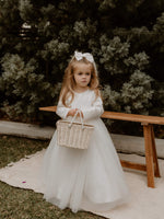 Lucy flower girl dress for winter is worn by a young flower girl. She holds a basket and wears a satin bow girls hair accessory.