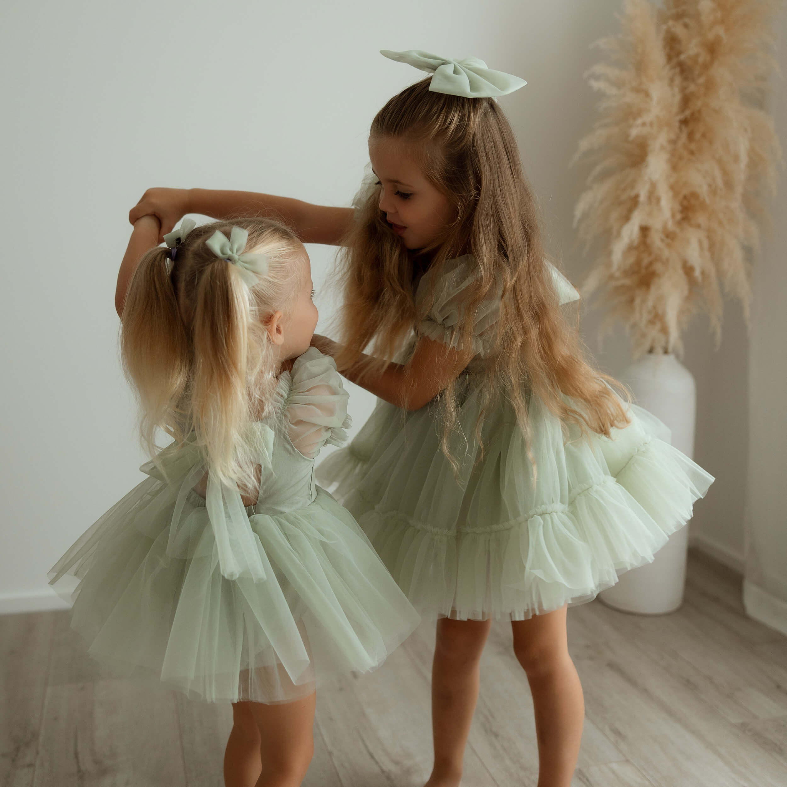 Matching sage green tulle dresses are worn by two young girls.