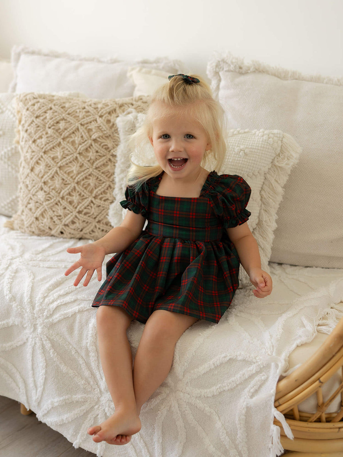 A toddler smiles wearing our Mila Christmas romper in Christmas plaid.