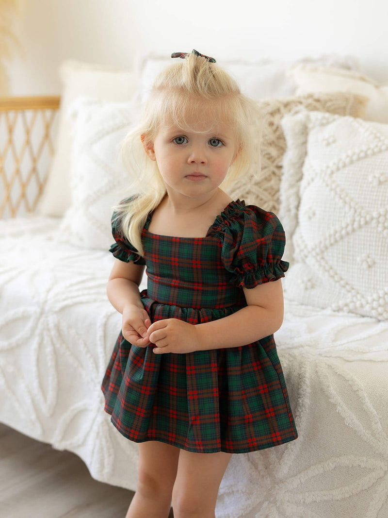 A toddler girl wears our Mila Christmas romper, a tartan romper with puff sleeves.