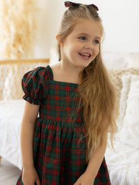 A young girl smiles wearing our Mila girls Christmas dress in Christmas plaid.