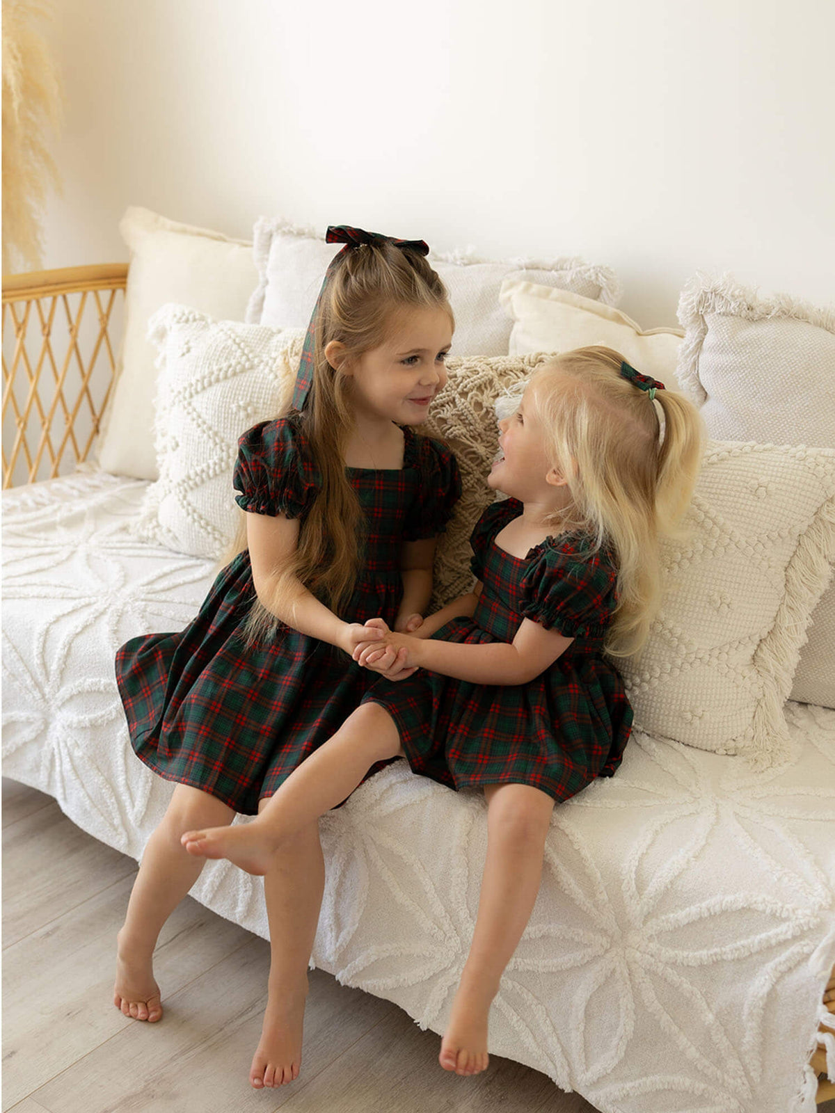 Sisters hold hands wearing our Mila Christmas dress and Mila tartan baby romper.