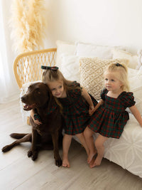 Sister and their dog sit all wearing matching Christmas plaid from our Christmas collection.