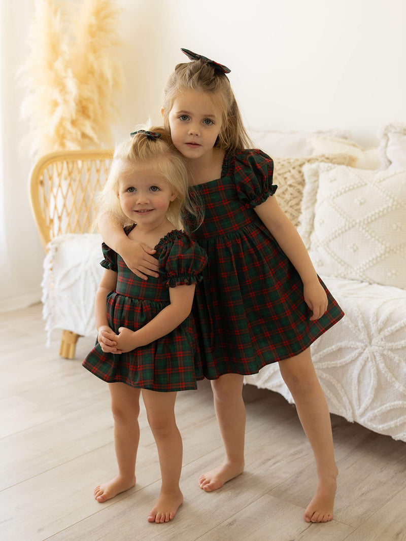 Sisters wearing our Mila girls Christmas dress and matching Mila girls Christmas romper in Christmas plaid print.