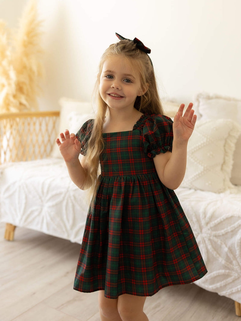 A young girl wears our Mila tartan Christmas dress and matching tartan bow.