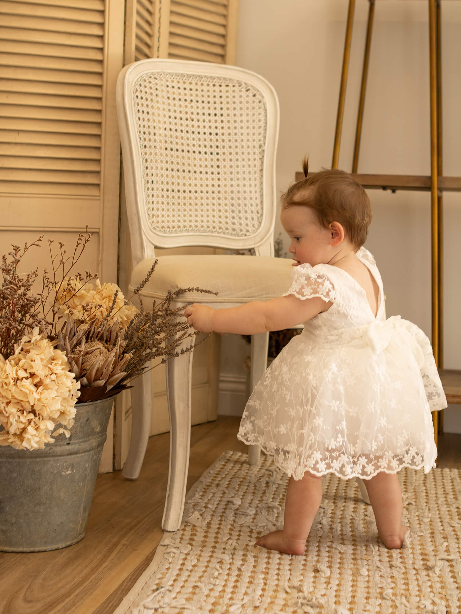 Lace baby flower girl romper is worn by a toddler who is playing with a bucket of flowers.
