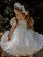 Pippa floral lace flower girl dress is worn by a young girl. She also wears a flower crown of ivory roses in her hair.