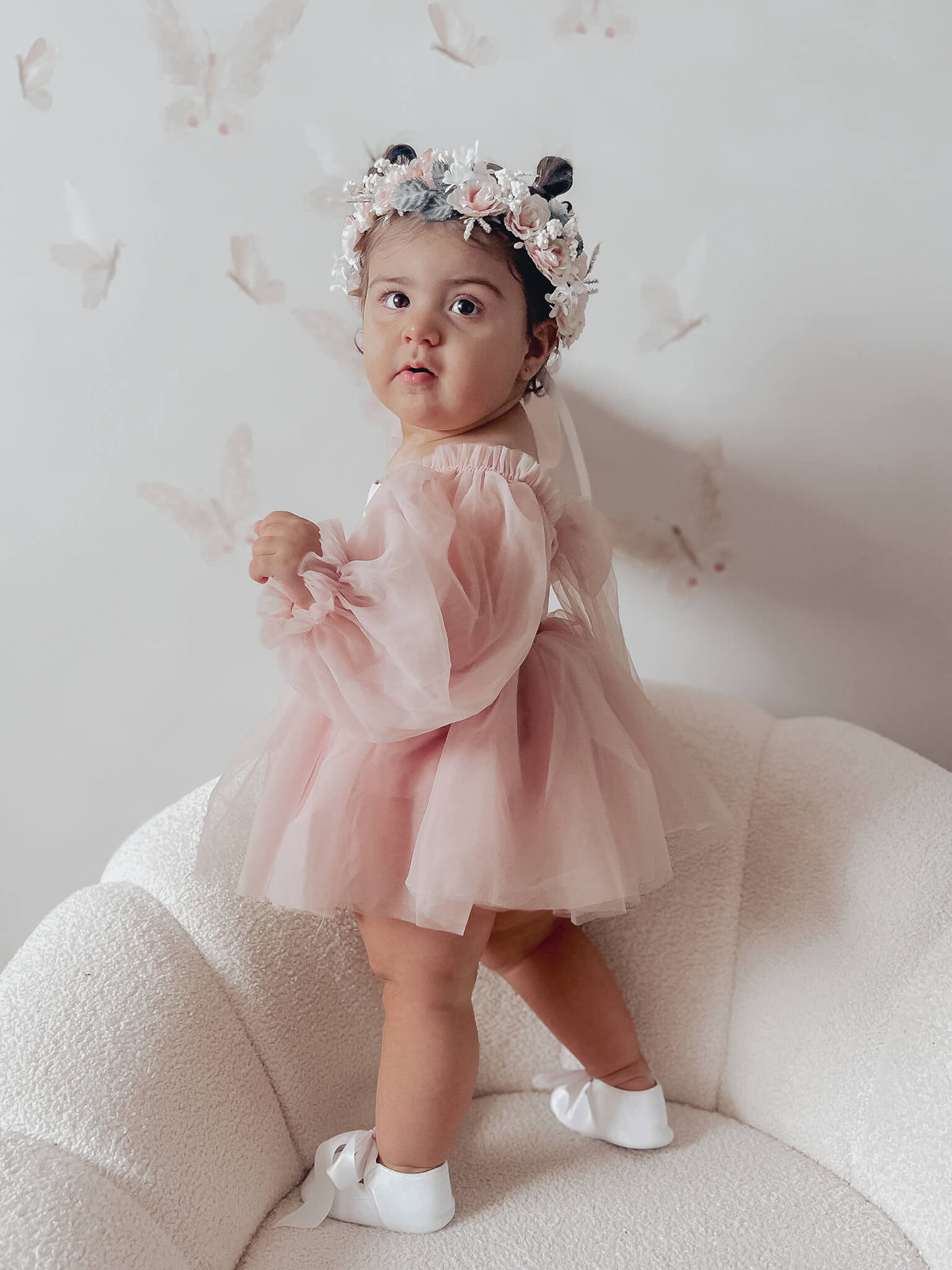 Wren baby flower girl dress in dusty pink is worn by a toddler who stands showing the dress from the side.