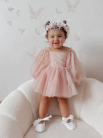 Wren baby flower girl dress with full length tulle sleeves is worn by a toddler. She stands showing the knee length soft tulle skirt and full length soft tulle sleeves.