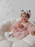 Wren flower girl romper for babies in dusty pink is worn by a toddler. She wears a girls flower crown with blush roses also.