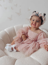 Toddler sits wearing our Wren baby flower girl romper in dusty pink. With full length tulle sleeves and tulle skirt. She also wears our Rose girls flower crown in blush.