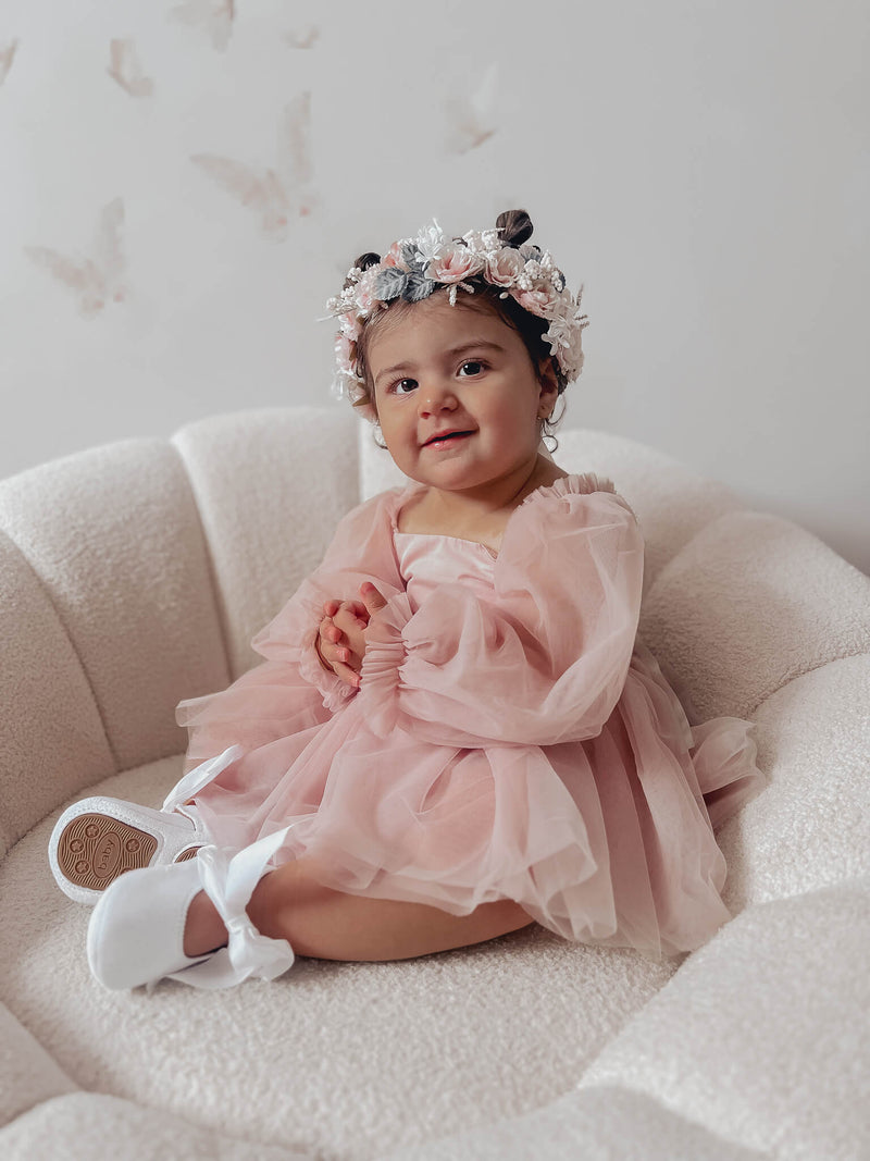 Wren flower girl romper in dusty pink is worn by a toddler, along with a matching flower crown.