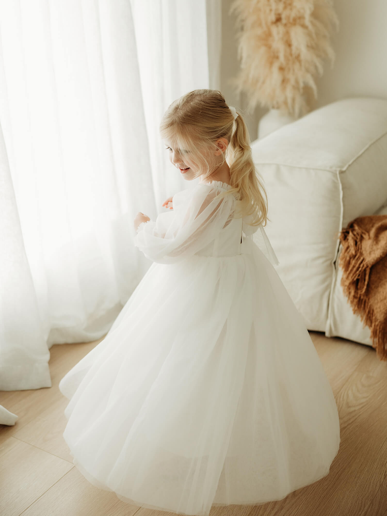 A young girl twirls wearing a full length flower girl dress in ivory.