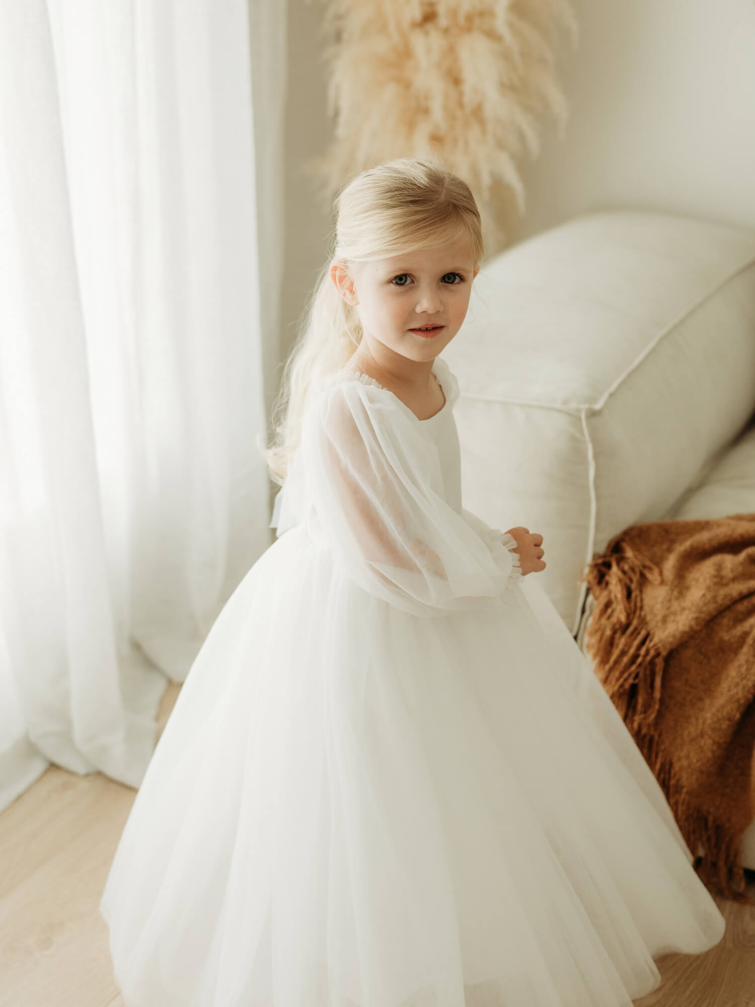 Full length ivory flower girl dress with tulle sleeves is worn by a young girl who is twirling.