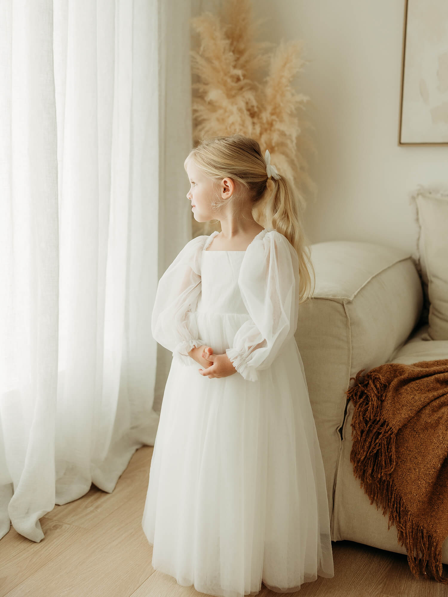Wren full length ivory flower girl dress with tulle sleeves is worn by a young girl.