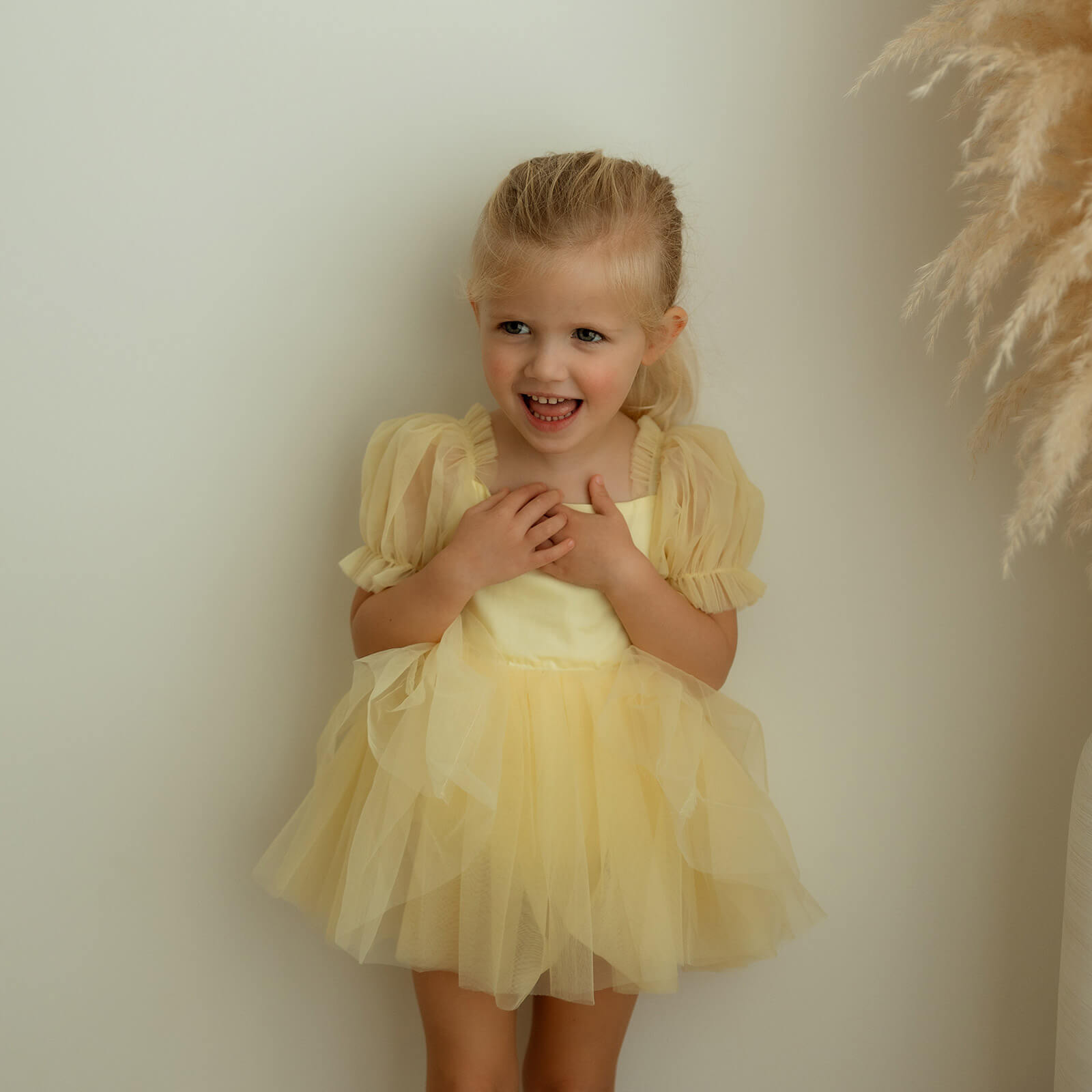 A little girl wears a yellow tulle party dress with puff sleeves.