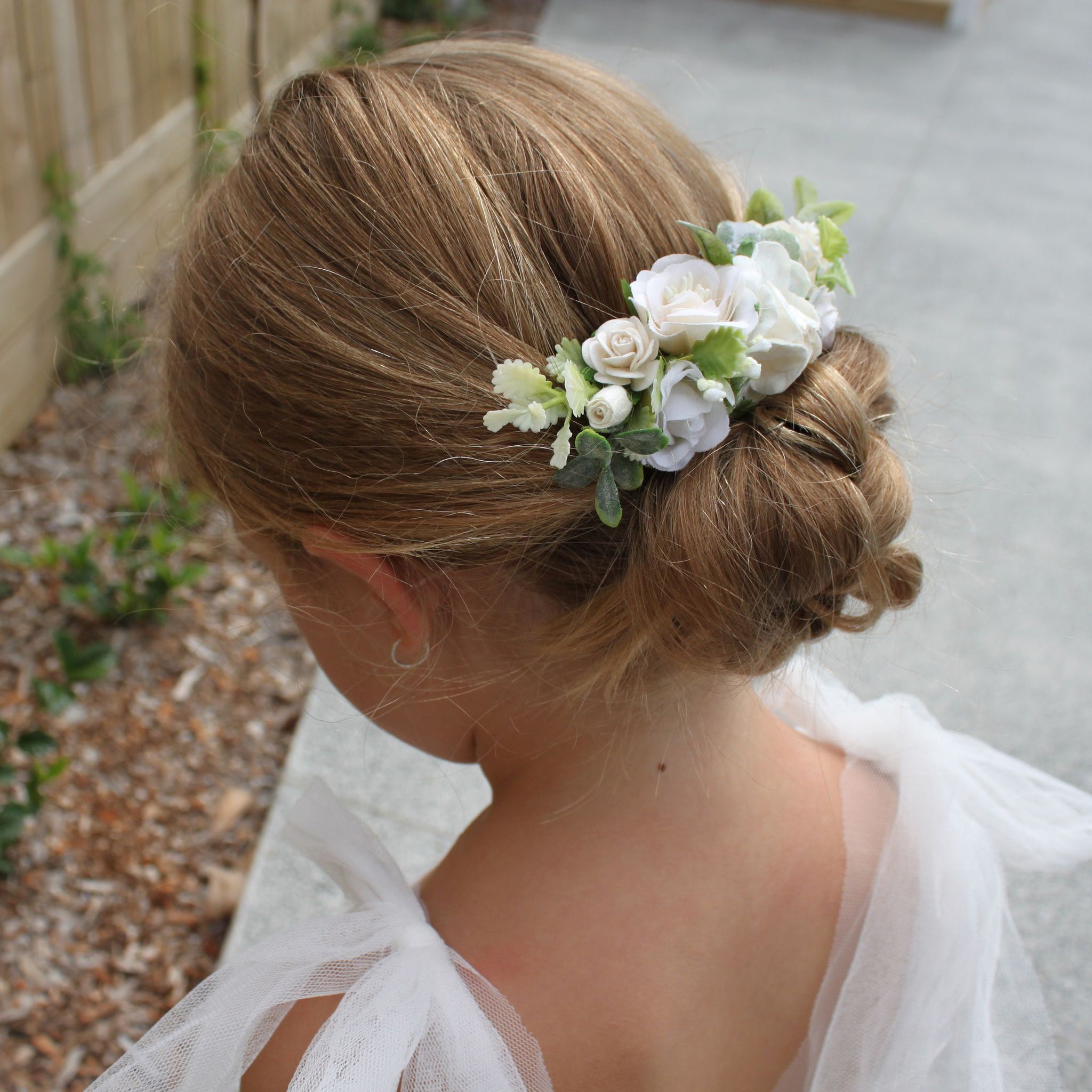 Ava girls ivory floral comb being worn by a young flower girl. She wears a low wedding up-do with the comb centered above it.