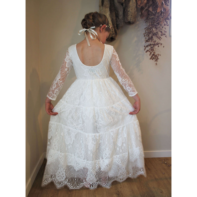Full length lace flower girl dress being worn by a girl, shown from behind. Showing the lined scoop back and tiered lace with eyelash detail.