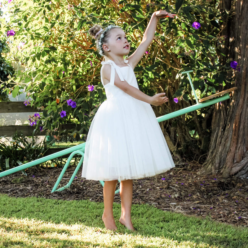 Young girl dances in our Margot tea length flower girl dress. This is an ivory girls dress, with a tulle tea length skirt. She also wears our Eden flower crown.