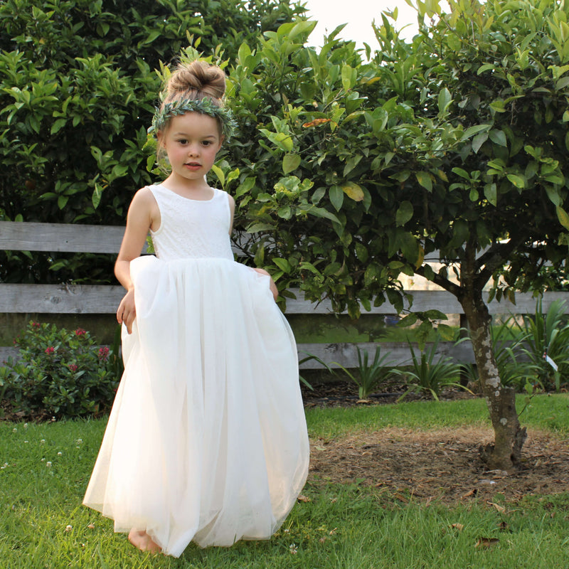 Young girl wears our Mia light ivory flower girl dress, with a sleeveless lace bodice and full ivory tulle skirt. She also wears our Olive flower crown.