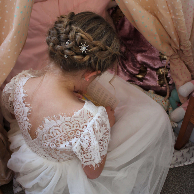 Poppy tea length flower girl dress worn by a young girl with star clips in her hair. Showing the lace feature back of the dress.