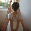 Poppy flower girl dress being worn by a girl, shown from behind. It has a lace bodice, lace flutter sleeves and a tea length tulle skirt.