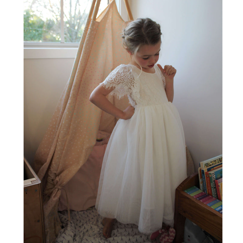 Poppy flower girl dress in ivory is worn by a young girl. The skirt is tea length ivory tulle and the bodice is ivory lace, with lace flutter sleeves.