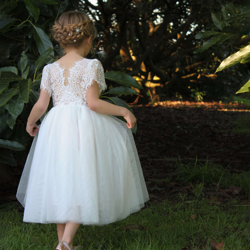 Poppy ivory flower girl dress on a young girl who is walking outside. Showing the feature eyelash lace back, and tea length ivory tulle skirt.