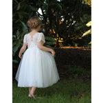 Poppy ivory tea length flower girl dress being worn by a young girl as she walks outside.