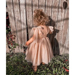 Rosie flower girl dress shown from the back, worn by a toddler. It is champagne in colour with tulle bow straps and a tulle skirt.