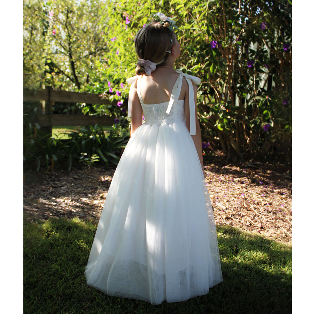 Sonnet ivory flower girl dress worn by a young girl, along with our Grace girls flower crown. She stands in a garden in the full length tulle flower girl dress.