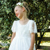 Young flower girl laughs wearing our Violette white flower girl dress, which is full length lace. Along with our Delilah floral headband, girls flower girl flower crown.