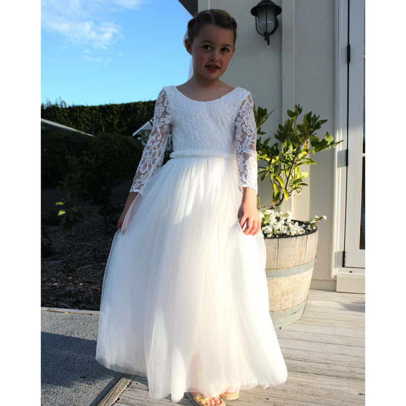 Belle ivory flower girl dress with long sleeves and full length tulle skirt worn by a young girl.