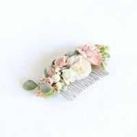 Side view of Emma girls floral hair comb accessory, showing details of ivory and dusty pink flowers, with greenery and gold accents upon a silver hair comb.