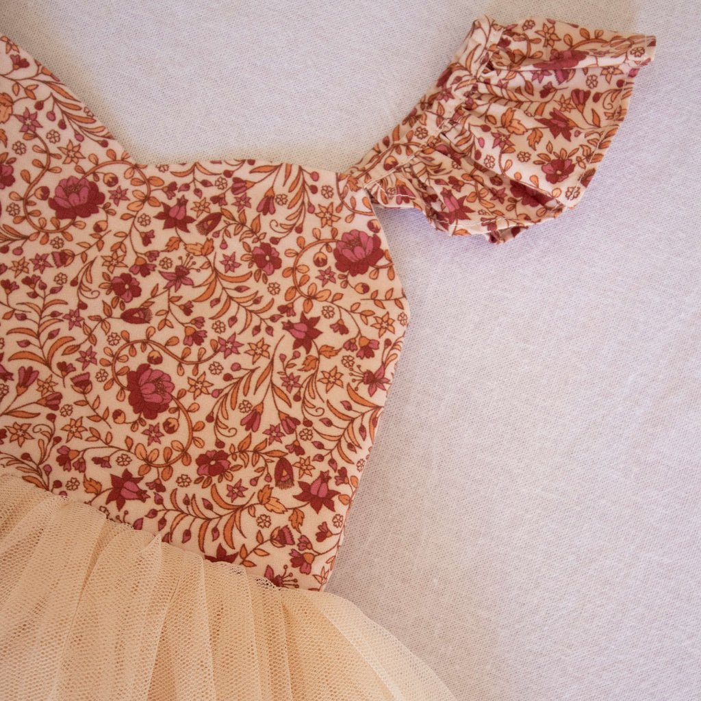 Everly tulle baby romper is worn by a toddler. The romper has a cotton floral bodice and a light cream tulle skirt.
