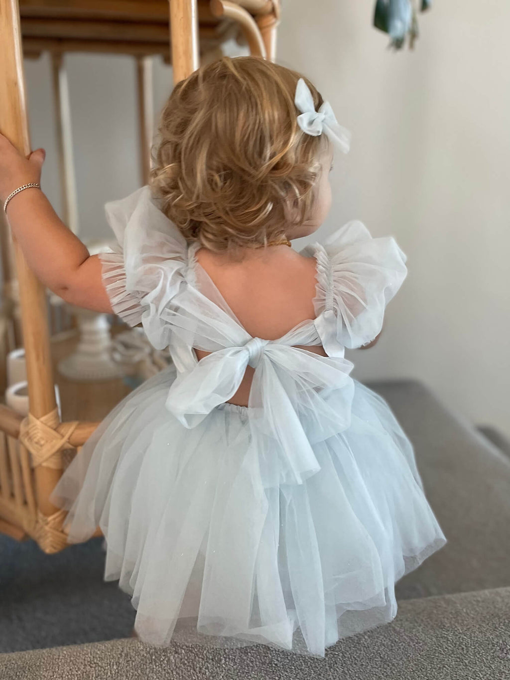 Gabrielle baby flower girl dress is worn by a toddler, in colour dusty blue, along with matching tulle pigtail bows in her hair.
