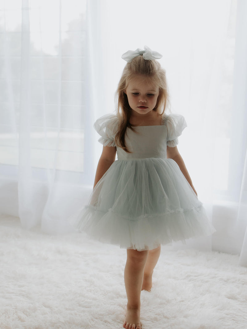 Gabrielle dusty blue flower girl dress with tulle puff sleeves, is worn by a young girl, she also wears a tulle bow in her hair.