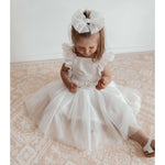 A young girl wears our Gigi ivory flower girl dress and our tulle bow in her hair.