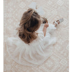 A young girl sits on the floor holding a basket of flowers, she wears our Gigi white flower girl dress.