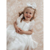 A young girl laughs laying on the floor, wearing our Gigi flower girl dress and ivory tulle bow.